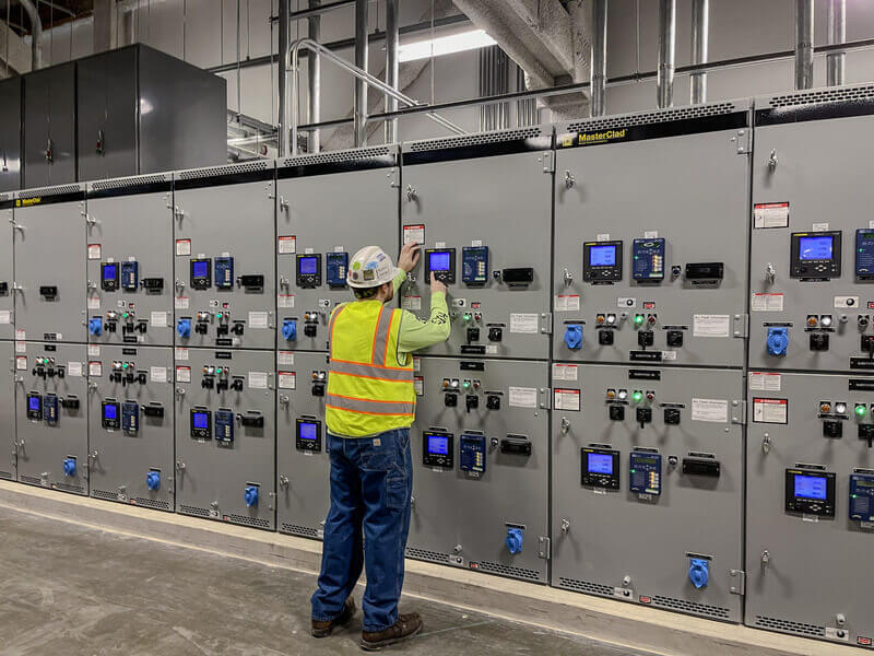 technician inspecting electrical switchgear panel in facility